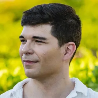 Pier-Luc Charbonneau de profil, cheveux foncés courts et chemise blanche, sur un fond vert flou.